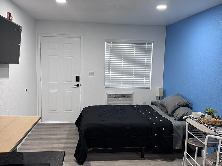 Furnished bedroom with a full bed, accent wall, and window A/C unit for added comfort and privacy.