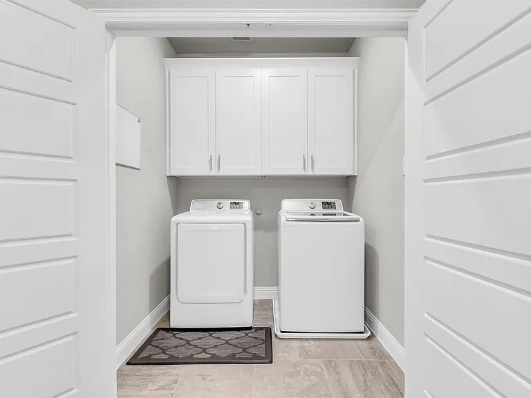 Dedicated laundry area featuring white shaker-style cabinetry with brushed nickel hardware, light grey wall paint, and wood-finish flooring