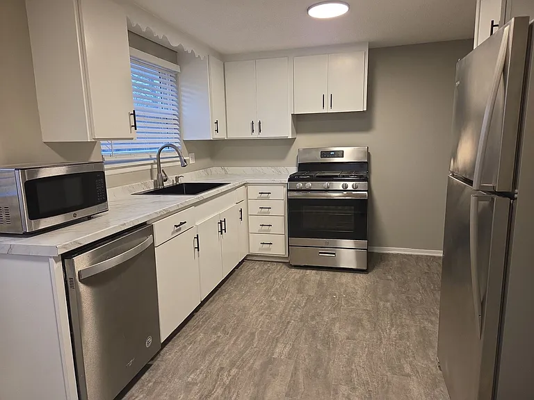 Bright kitchen with updated countertops, white cabinetry, stainless refrigerator and range, and dishwasher.