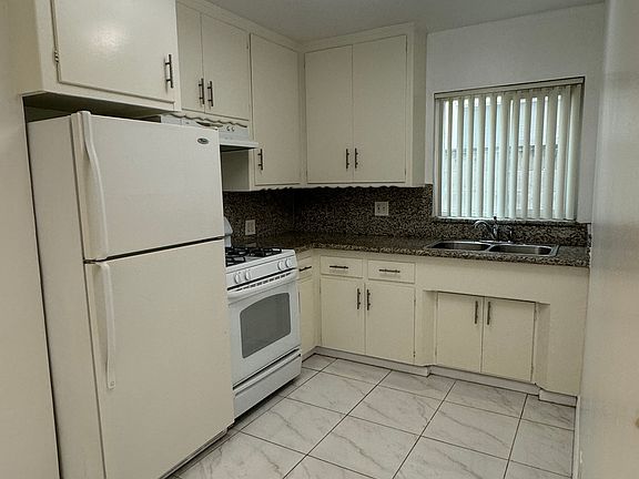 Closer look at the kitchen with refrigerator, gas stove and double sink.