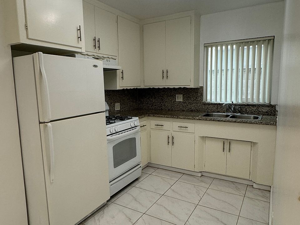 Closer look at the kitchen with refrigerator, gas stove and double sink.