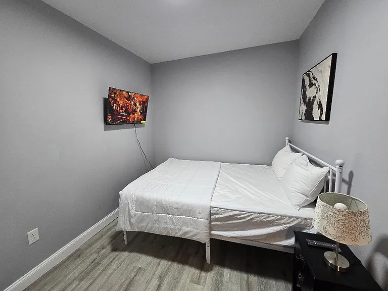 Private bedroom with a full bed, bedside table and lamp, wall-mounted TV, and durable wood-look flooring.