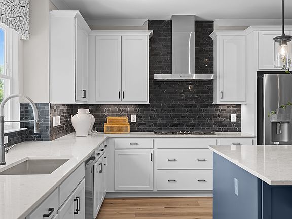 A modern, well-designed kitchen with white cabinets, a black brick backsplash, and a blue island cou