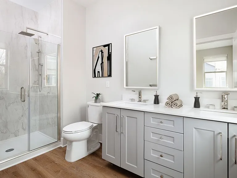 Signature Collection bath with white quartz countertop, grey cabinetry, lighted vanity mirrors, porcelain shower surround, and hard surface flooring
