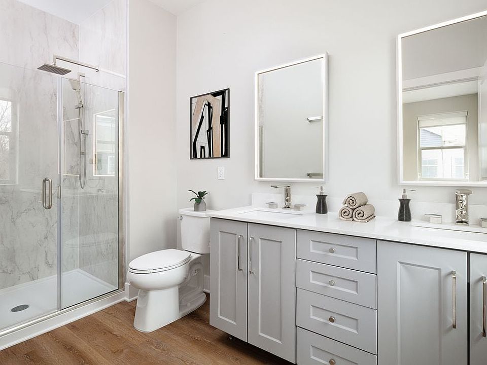 Signature Collection bath with white quartz countertop, grey cabinetry, lighted vanity mirrors, porcelain shower surround, and hard surface flooring (Representative photo)