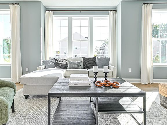 Spacious and bright living room with box bay window between 2 large windows, light wood floors.