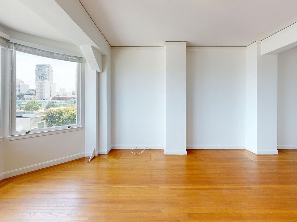 Spacious room with hardwood floors and large windows overlooking city skyline