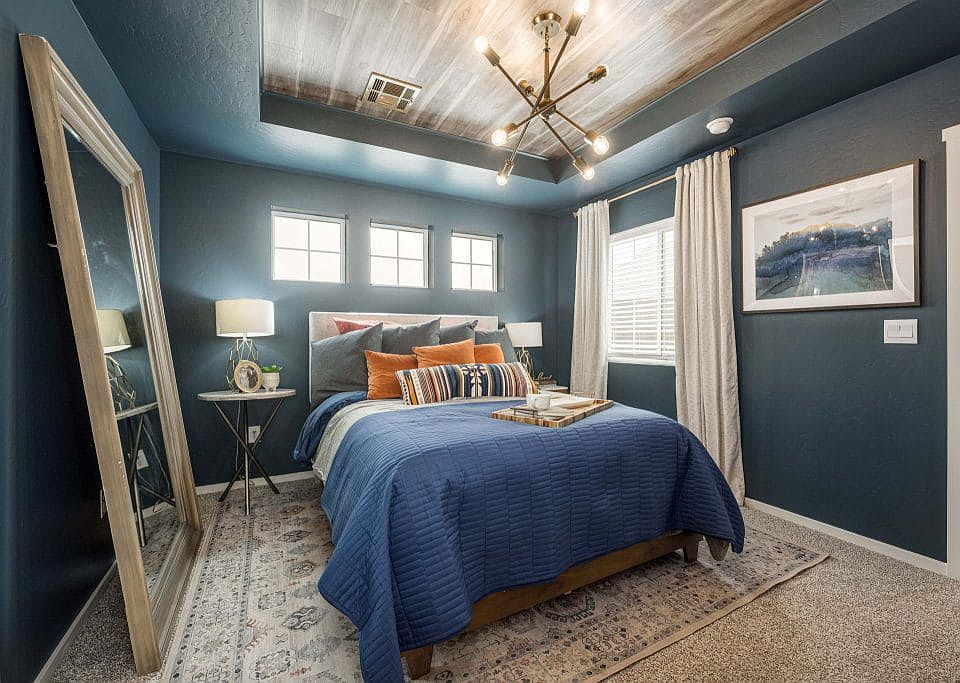 A cozy bedroom with dark blue walls, a wood-paneled ceiling, a modern chandelier, a bed with blue an