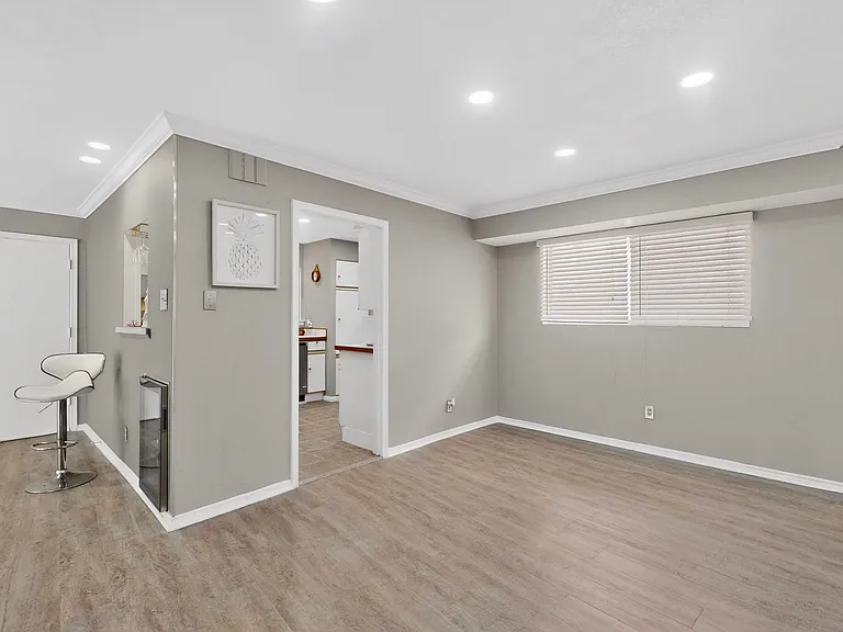 A bright dining area with a wooden floor and a window beside the enclosed kitchen space.
