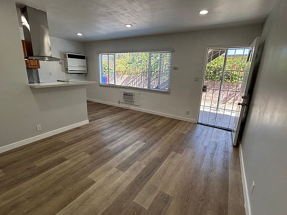 Living room, kitchen on the left, natural light from window, front door on the right