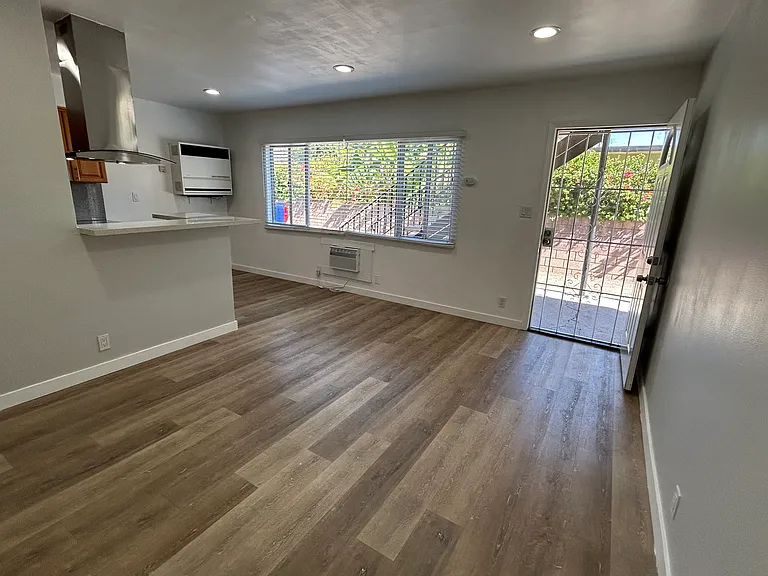 Living room, kitchen on the left, natural light from window, front door on the right