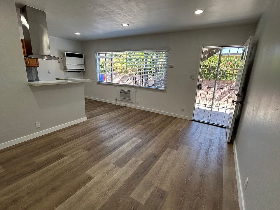 Living room, kitchen on the left, natural light from window, front door on the right