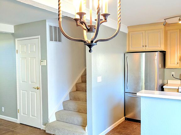 Open dining space with modern light fixture, tile flooring, and direct sightlines into the kitchen featuring stainless appliances. Carpeted stairs lead to the upper level.