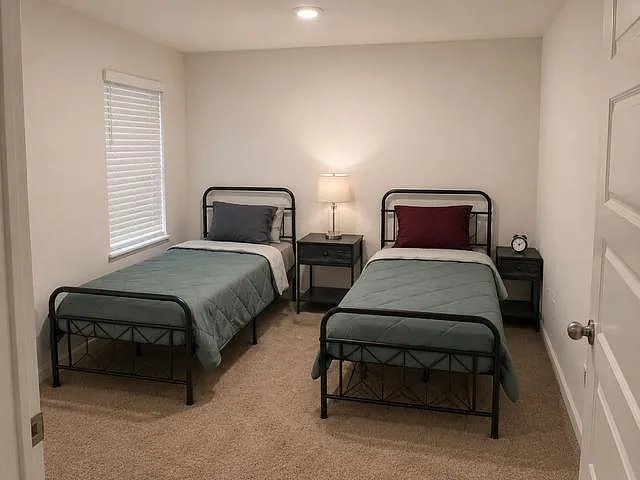 45 bedroom with two twin beds, matching nightstands, and a window with blinds for privacy and comfort. Single adults