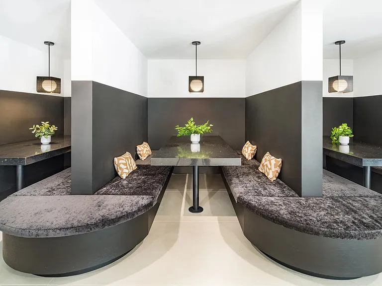 Semi-private dining booths with curved banquette seating, pendant lighting, and intimate table settings suited for casual meals, work sessions, or conversation.