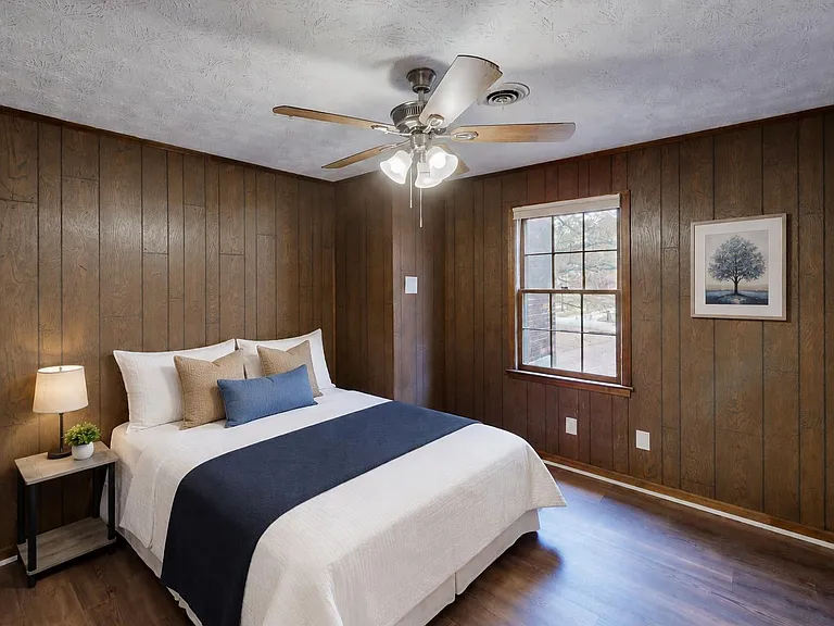 Private bedroom with wood-paneled walls, ceiling fan light, and a window for natural light and ventilation.