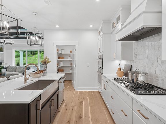 A modern, open-concept kitchen with white cabinets, a marble countertop, and a gas stove, leading in
