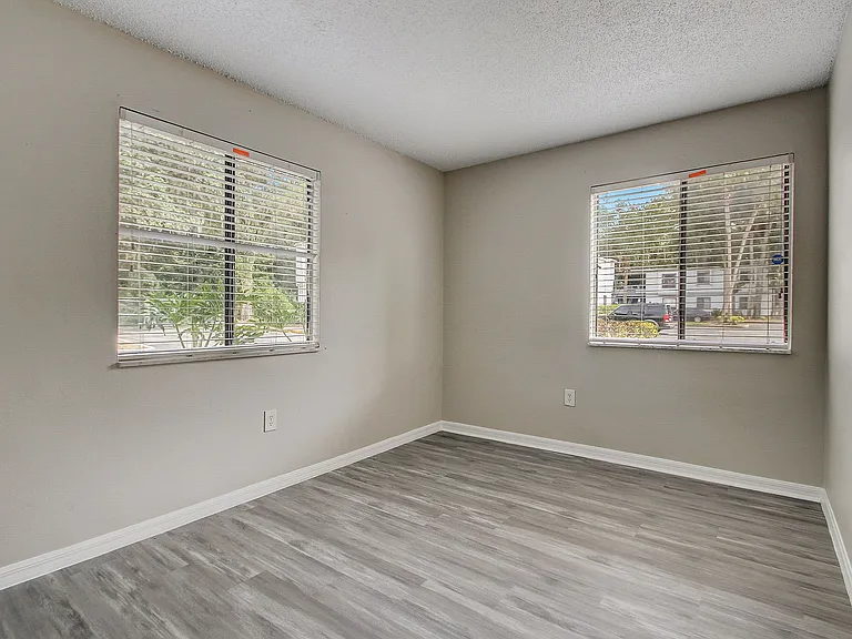 Bright and airy room with modern gray flooring and large windows offering a pleasant outdoor view.