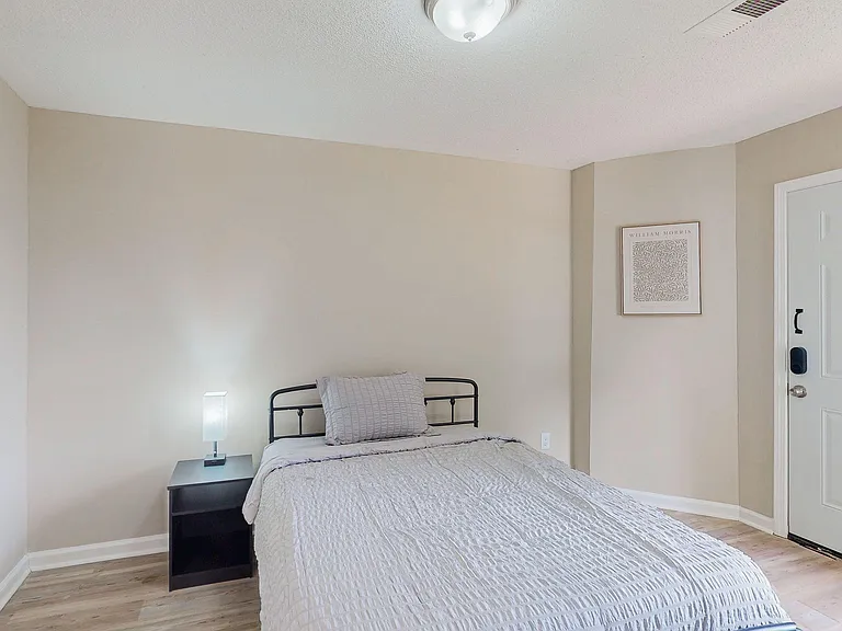 Furnished bedroom with a full-size bed, nightstand lighting, and a private entry door for easy access.
