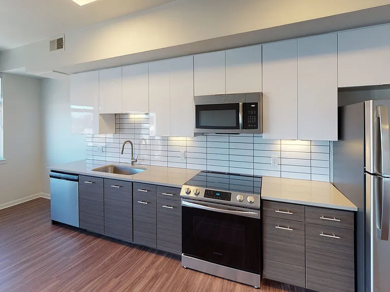Apartment kitchen with stainless steel appliances, quartz countertops and wood-style flooring.