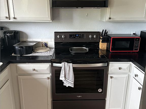Efficient kitchen workspace with ample cabinetry, generous counters, and a full-size electric range plus microwave.