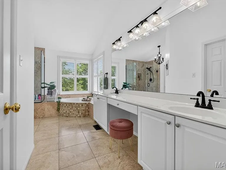 Spacious bathroom featuring a double vanity with ample counter space, a large built-in mirror, a soaking tub with mosaic tile surround, and a separate glass-enclosed shower