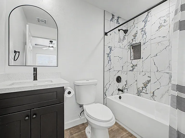 Updated bathroom with a single-sink vanity, arched mirror, and tub/shower with full-height tile surround and built-in niche.
