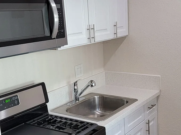 Stainless steel appliances including gas range, microwave, refrigerator and white cabinets in kitchen at Orlando Woods Apartments in El Cajoon, California.