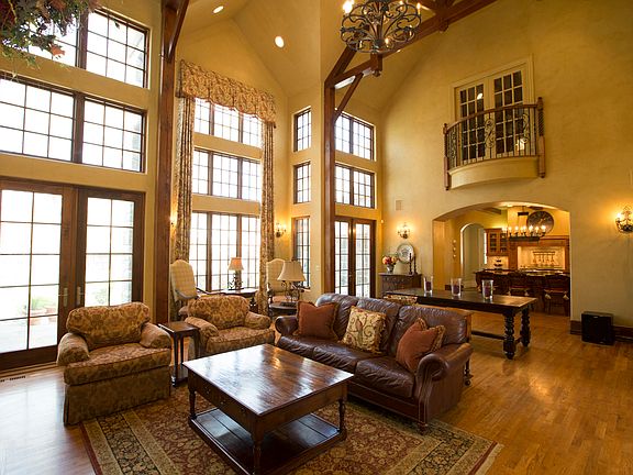 Natural light fills the massive Great Room with an old world inspired ambiance highlighted by a beautiful wall of floor to ceiling windows and French doors, two Juliet balconies, soaring beamed ceiling, hand finished glazed walls and rich hardwood floors.