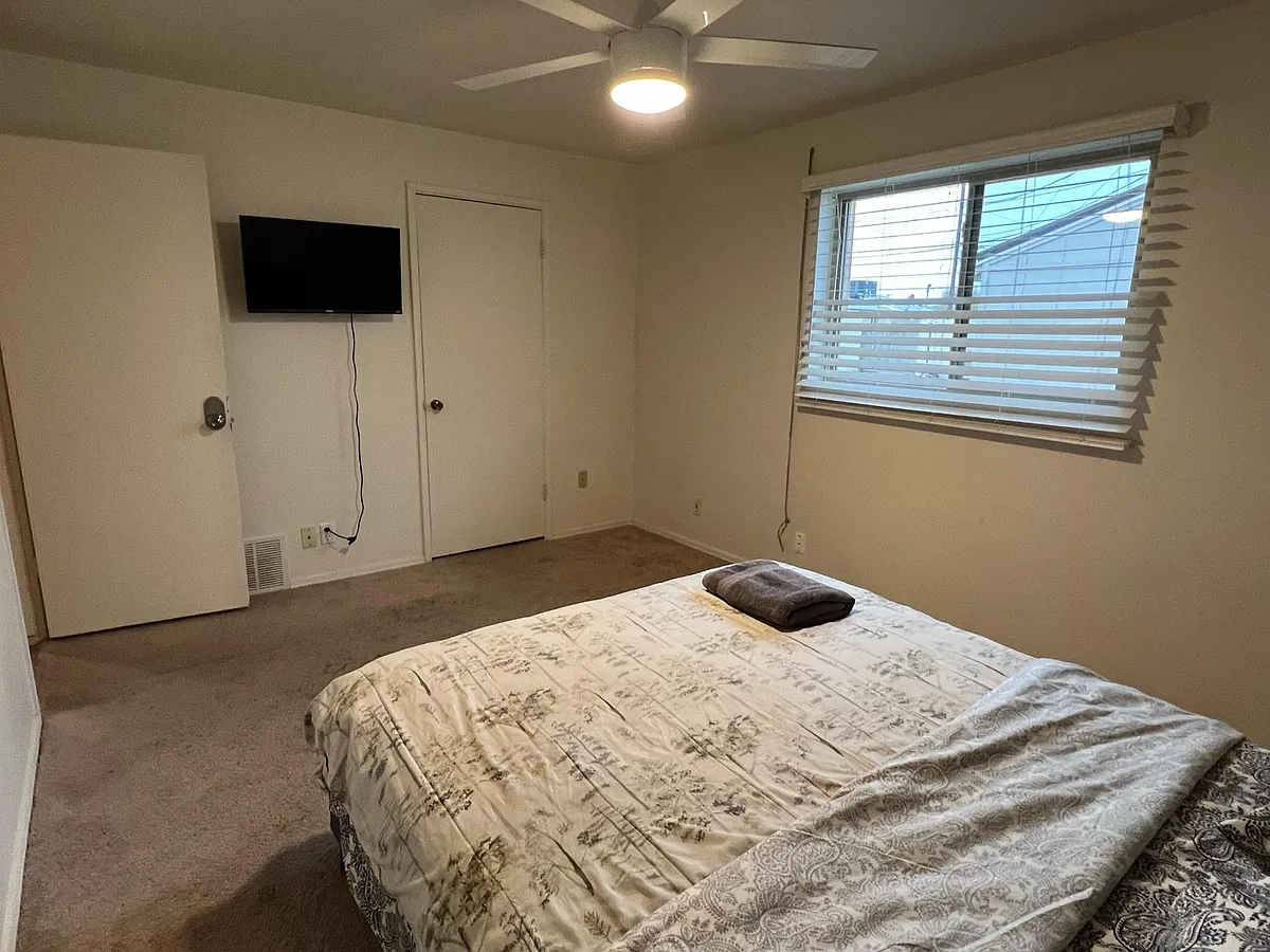 Private bedroom with carpeted flooring, ceiling fan, window with blinds, and a wall-mounted TV for easy relaxing. - N 17th St