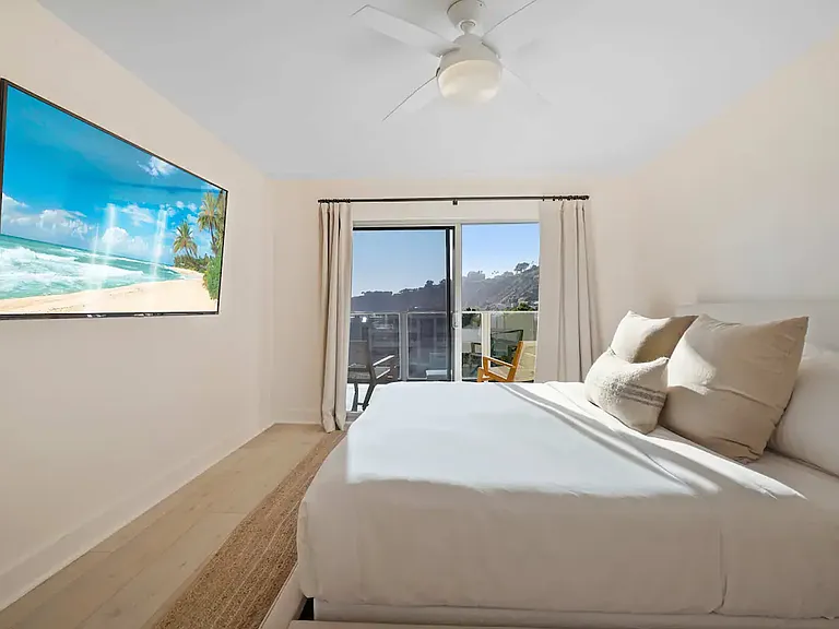 Relax in a well-appointed bedroom featuring plush bedding and a large wall-mounted TV.
