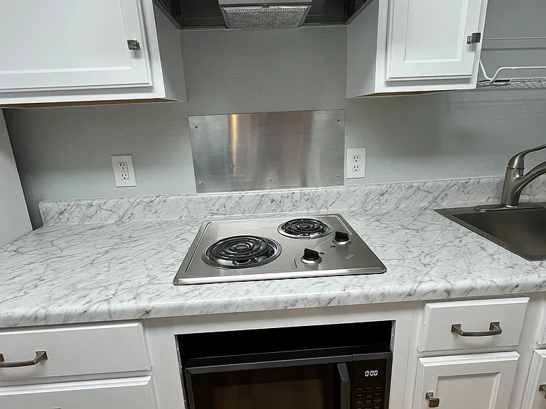 Detail of kitchen appliance. Two burner electric stove, vent-a-hood light combo, and microwave/air fryer combo.