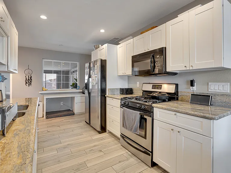 Bright kitchen featuring stainless steel appliances, gas stove, granite countertops, and white cabinetry