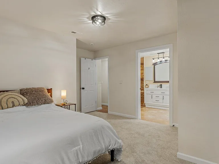 Spacious carpeted bedroom with a double bed setup and convenient access to an adjacent vanity bathroom area.