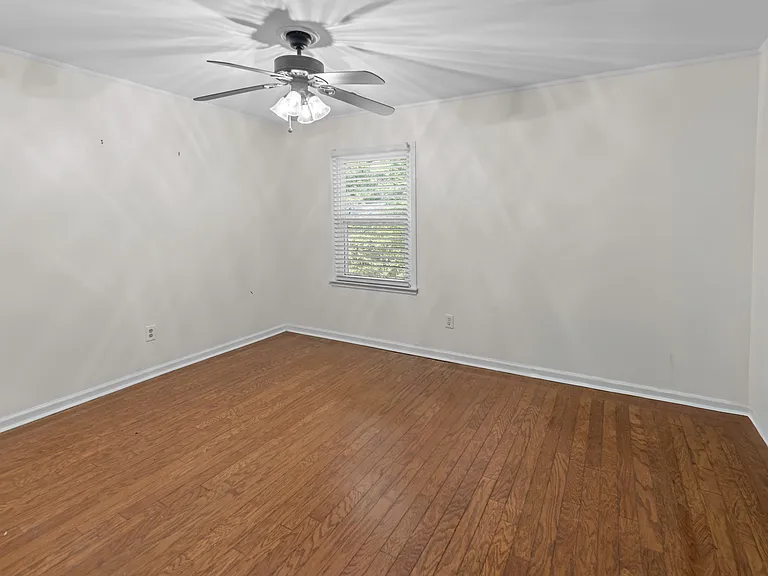 Well-proportioned bedroom with rich hardwood floors, ceiling fan, and garden-view window _ comfortable and move-in ready.