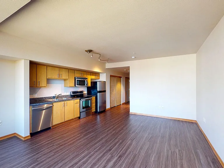 Apartment kitchen with stainless steel appliances, dining and living room with wood-style flooring.