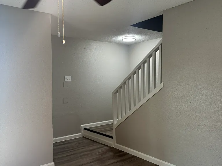 This bright entry space features modern wood_style flooring, a sleek ceiling fan, and a clean, open layout leading to the upper level.
