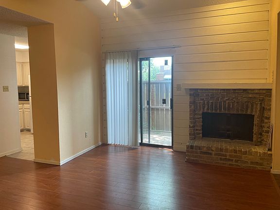 living area has patio door, wood burning fire place, soaring ceilings, ceiling fan and hard wood floors.