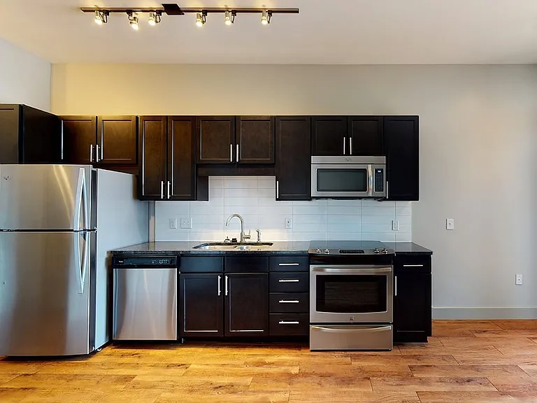 Apartment kitchen with stainless steel appliances, granite countertops and wood-style flooring.