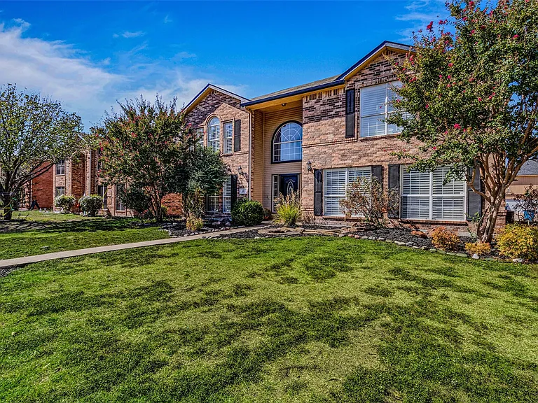 Brick exterior residence featuring prominent arch window, multiple large windows with shutters, and a manicured front lawn