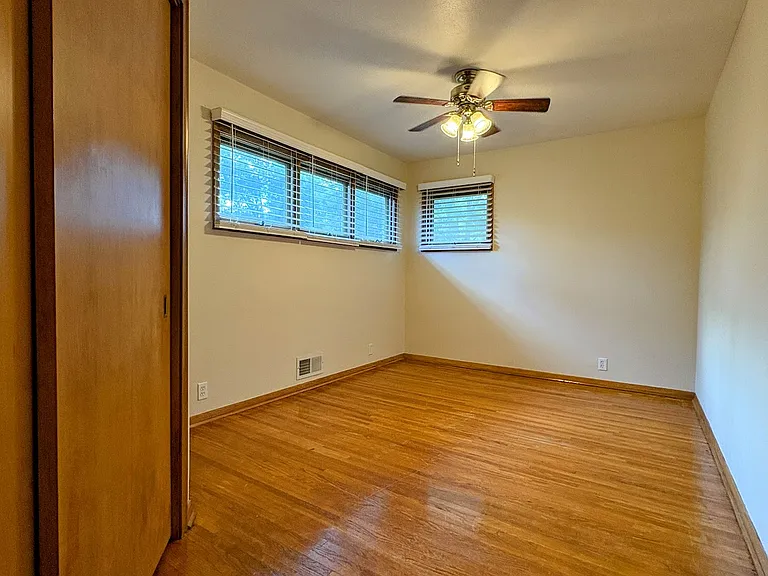 Relaxing primary bedroom. Hardwood floors. Ceiling fan. Raised awning-style windows provide privacy and invite in the sunshine.