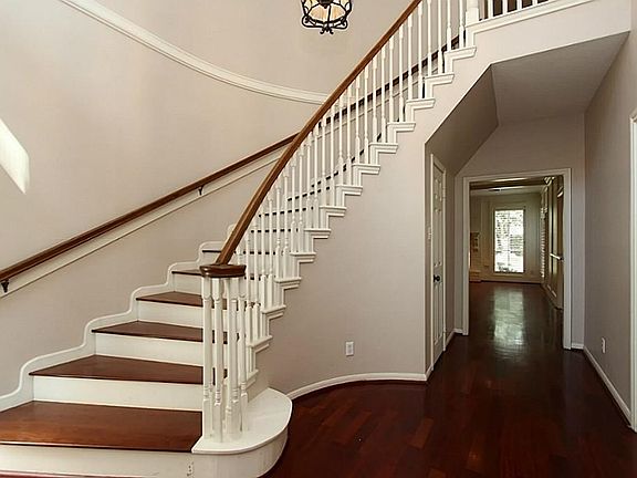 The stairway in the foyer has wood stairs and impressively winds to the second story bedrooms and game room. Down the hall is a view of windows looking onto backyard and pool.