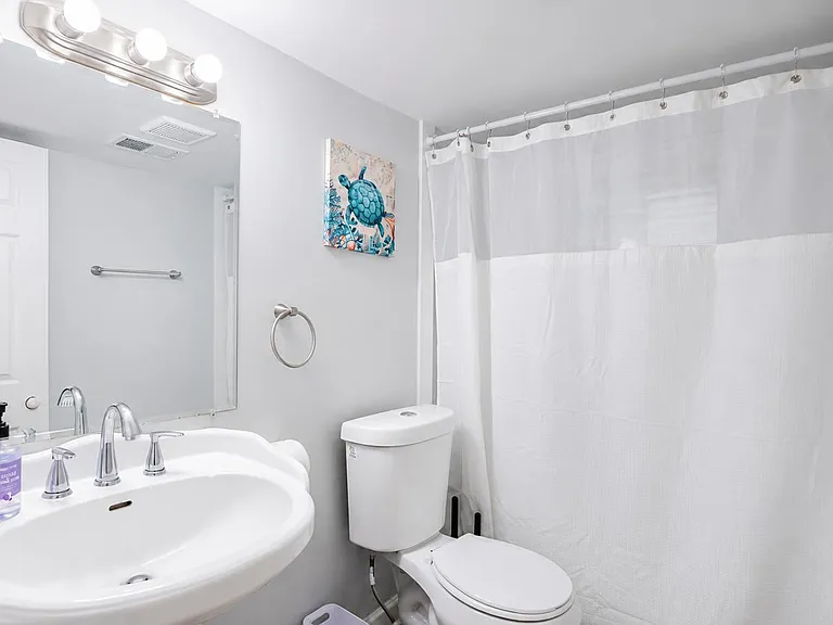 Clean full bathroom featuring a wide vanity with large mirror, updated lighting, and a tub/shower with curtain.