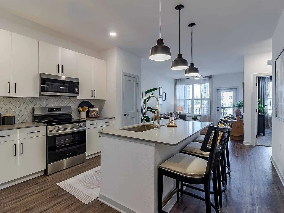 Cook and gather in the open-concept kitchen of the A1 floor plan, featuring a quartz island with seating, stainless steel appliances, and a herringbone tile backsplash.