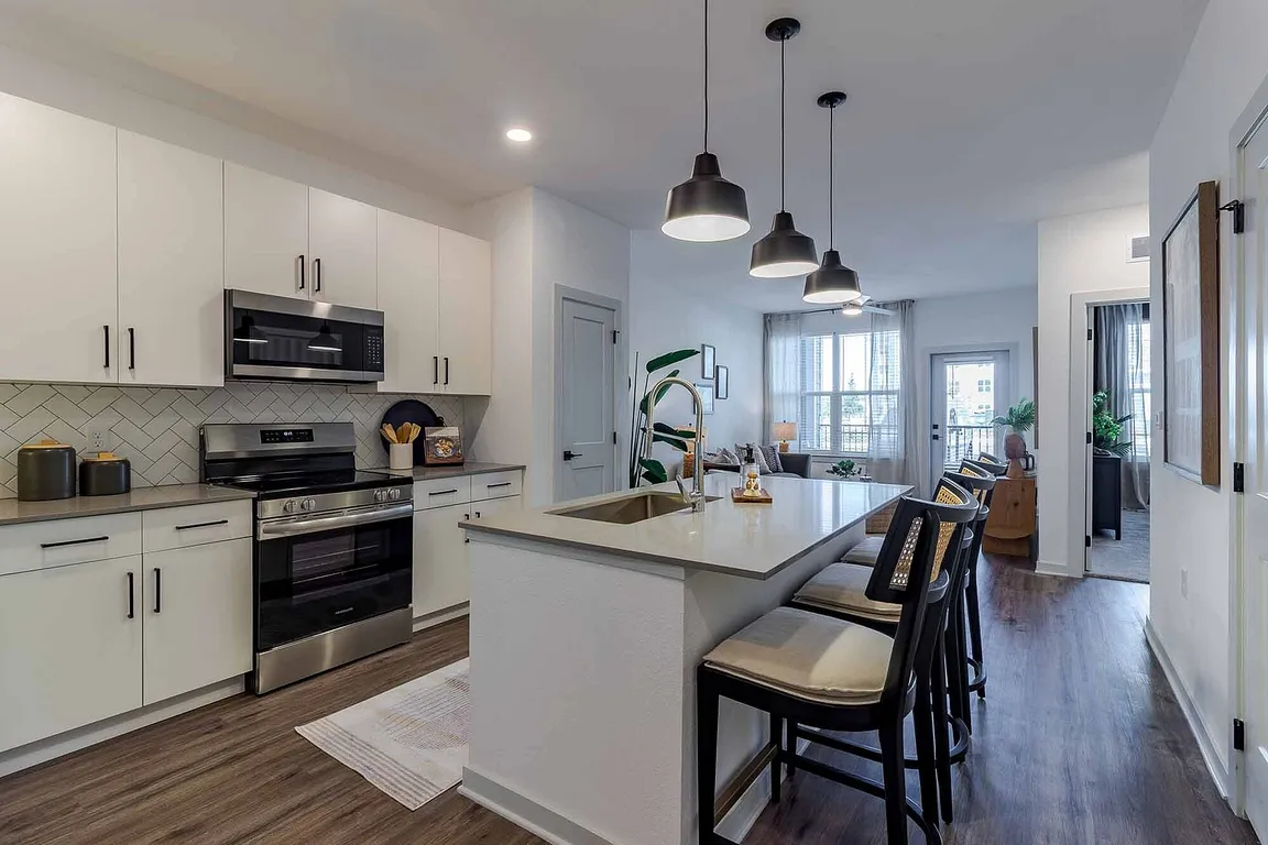 Cook and gather in the open-concept kitchen of the A1 floor plan, featuring a quartz island with seating, stainless steel appliances, and a herringbone tile backsplash.