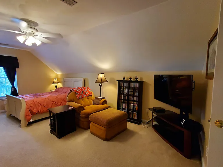 Front view of overstuffed Chair, ottoman, end table, media cabinet w/glass doors, corner TV stand w/glass shelves, bed and floor lamp.