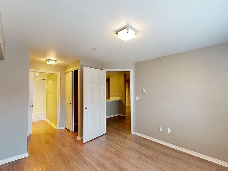 Spacious apartment bedroom with attached bathroom and wood-style flooring.