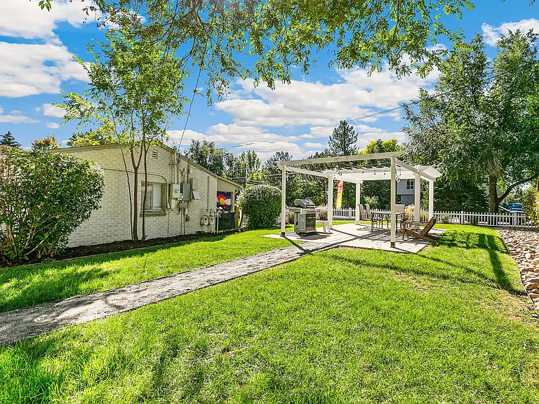 Charming backyard with lush green lawn, pergola-shaded patio, and cozy seating area perfect for outdoor relaxation.