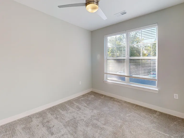 The Elm floor plan's bedroom features lush carpeting, a ceiling fan, and large windows with lots of natural light. The Elm floor plan's bedroom features lush carpeting, a ceiling fan, and large windows with lots of natural light.