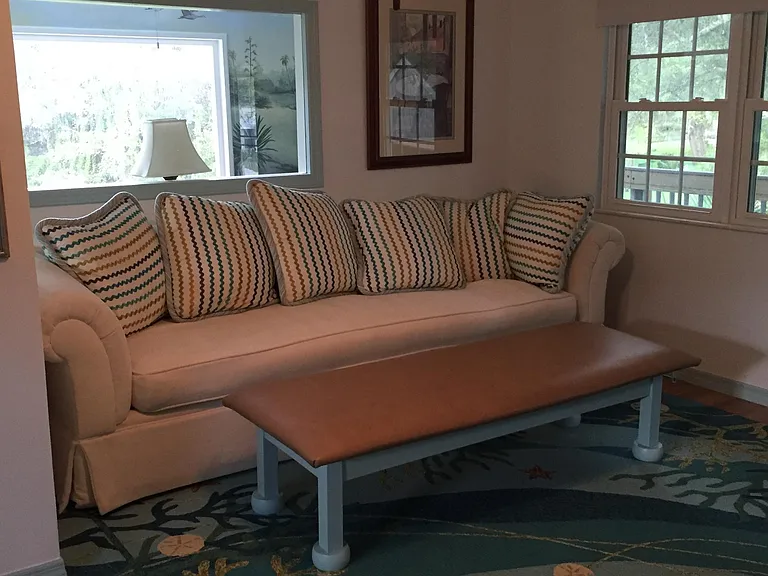 View from standing in front of TV to couch. Large window behind couch looks out through sunroom to picture windows out back